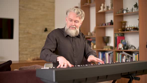Adult solid gray-haired man with a stylish beard plays the electronic piano