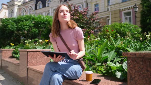Beautiful Young Woman Tourist with Takeout Coffee in the City Center Using Tablet Pc