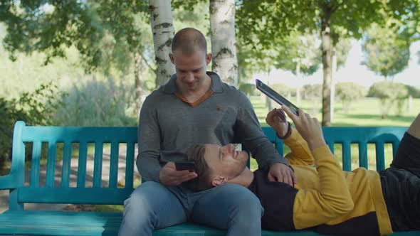 Gay Couple Relaxing with Digital Devices Outdoors