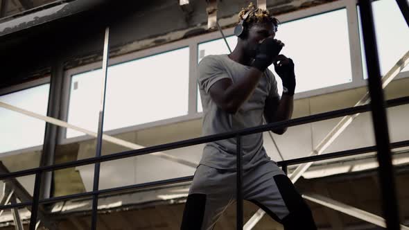 Young Male Boxer Practicing Shadow Boxing Around the Metal Structures Low Angle View