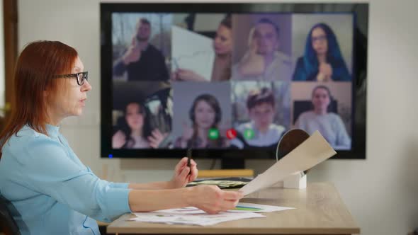 Serious Concentrated Female CEO Analyzing Papework Talking with Blurred Employees in Web Conference