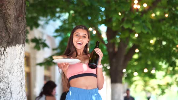 Young Woman Carries a Plate of Snacks and a Drink in Hands