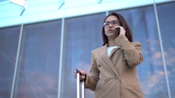 A Young Woman Stands Against the Background of a Business Center and Speaks on the Phone. Girl in a