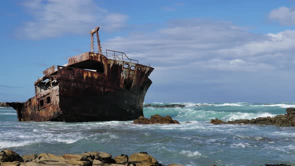 Old weathered shipreck in shallows with waves running in, rocky coastline of L'Agulhas, South Africa