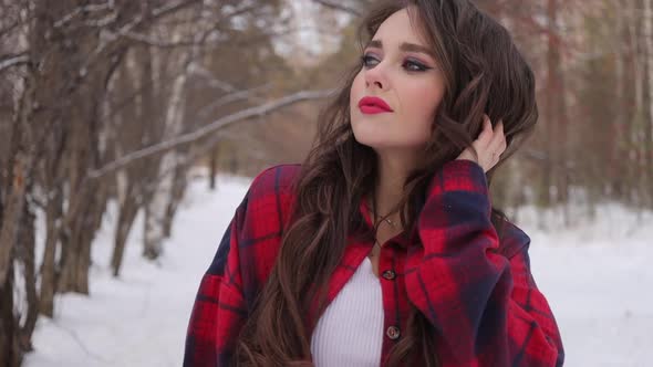 Young Woman with Wavy Hair Standing and Touching Face in Winter Forest