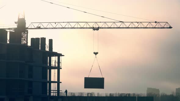 Working crane at the construction site against beautiful orange sunset