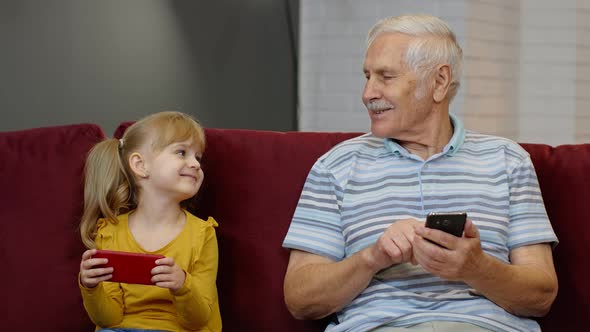 Senior Grandfather with Child Girl Granddaughter Using Digital Mobile Phone, Playing Games at Home