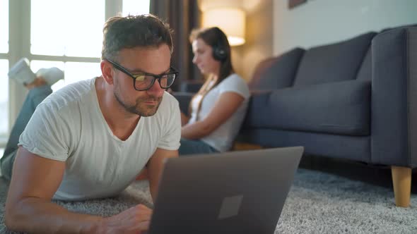 Couple Spends Time Together in a Cozy Room: Man Lies on a Carpet and Uses a Laptop, Woman with