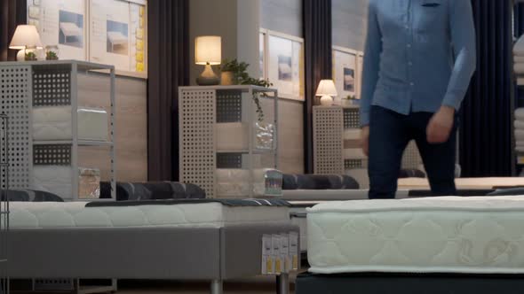 Male Customer Choosing Orthopedic Mattress and Bed at Furniture Store