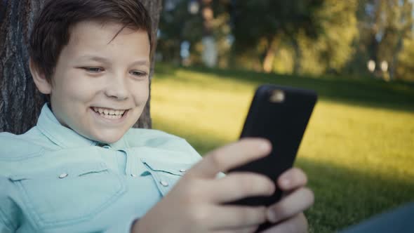 Teenager Playing Video Games on His Smartphone Outdoors