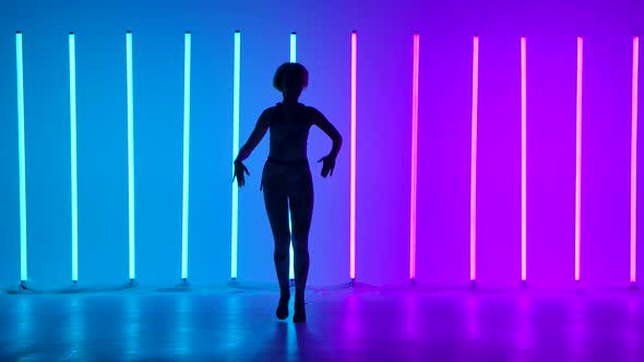 Silhouette of a Young Stylish Girl Dancing Against the Background of Multicolored Neon Tubes