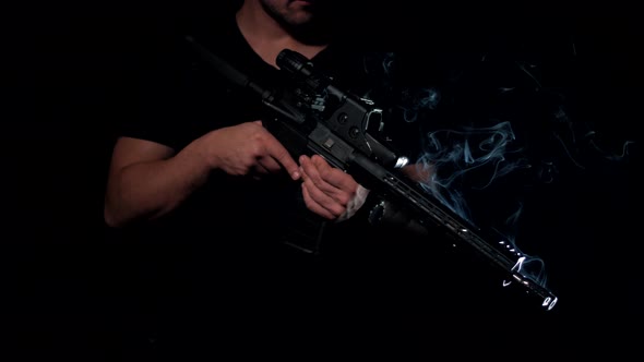Man holds an AR-15 carbine with a smoking barrel in his hands on a black background