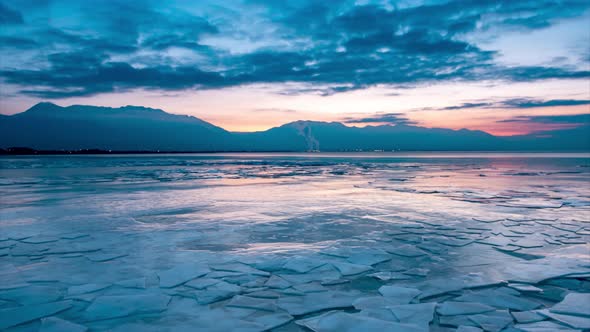 Sunrise time lapse with rafted ice on a frozen lake and mountains and a city in the distance