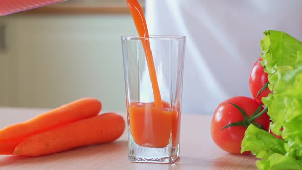 Woman Hand Pours Carrot Juice Into a Glass