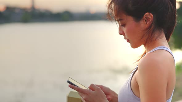 Portrait of asian young beautiful woman standing and looking at smartphone after exercise in park.