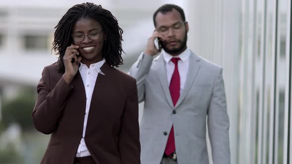 Confident Business People Talking on Smartphones While Walking