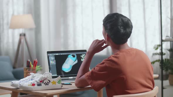 Asian Boy Footwear Designer Thinking Then Raising Index Finger While Designing Shoe On A Laptop