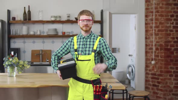 Repairman Hold Tool Box in Kitchen and Look at Camera