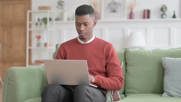 African Man Pointing towards Camera while using Laptop in Office