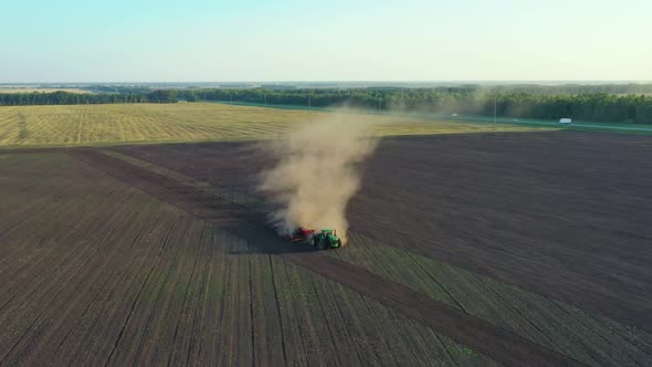 Green tractor cultivating ground and seeding a dry field.