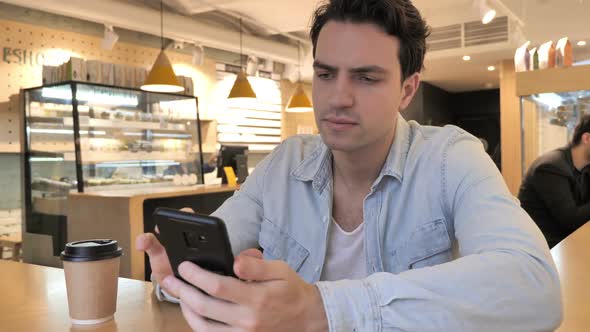 Young Man Upset By Online Loss of Work Sitting in Cafe