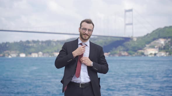 Businessman fixing tie by the sea.