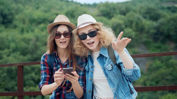 Two Female Travelers in the Mountains Discussing and Looking on a Smartphone During a Hike