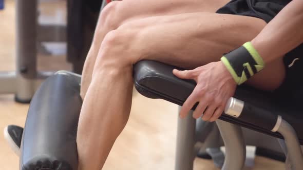 Closeup View of the Man Athlete with Muscular Legs Working Out at the Gym Leg Curl Trainer