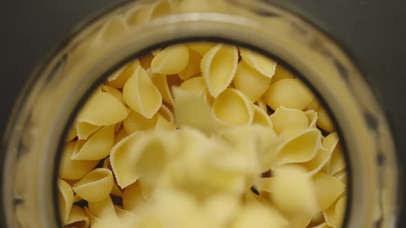 TOP VIEW: Uncooked Conchiglie Pasta Fall Into Glass Jar On Black Background - Slow Motion