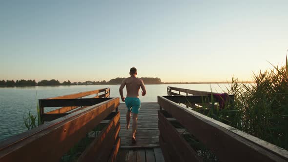 A Young Man is Running Down the Pier and Jumping Into the Lake in the Style of a Bomb