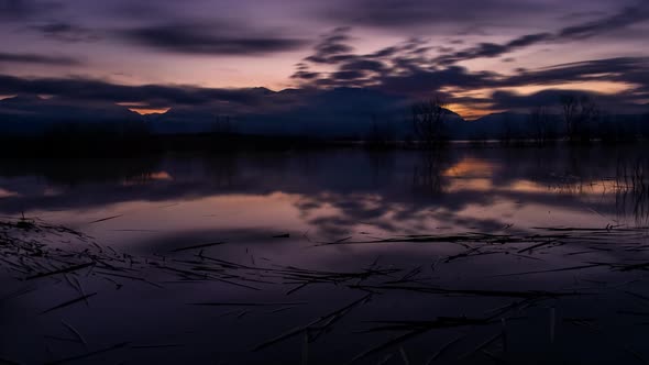 Dark to dawn time lapse of a lake with snow-capped mountains in the background and the sky reflectin