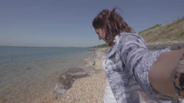 POV Shot Of Young Woman Reaching Down To Pick Up Plastic Bottle On Beach - Ungraded