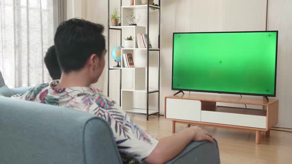 Asian Father And His Son Are Watching Green Mock-Up Screen Tv While Sitting On A Couch At Home