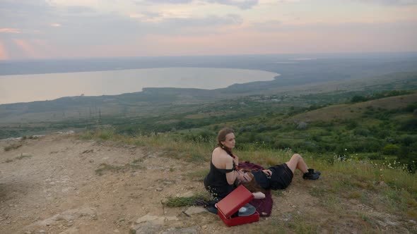 Two Hipster Girls Lie on the Ground in the Mountains and Listen To Music