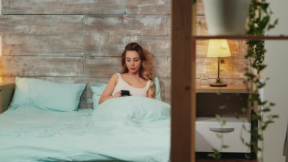 Beautiful Woman in Pajamas Yawning While Using Smartphone