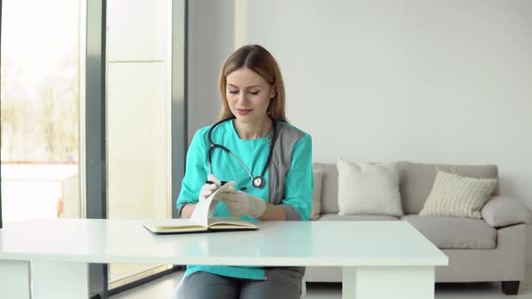 Female Doctor Wearing Medical Coat and Stethoscope Writes a Medical History in a Notebook