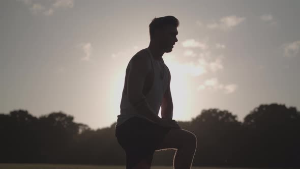 Man Stretching His Legs Before a Run Whilst Being Silhouetted By The Evening Sun - Ungraded