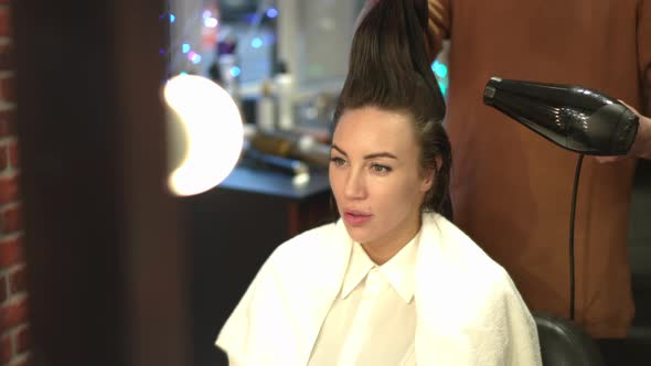 Reflection in Mirror of Confident Young Woman Sitting in Beauty Salon with Unrecognizable Tattooed