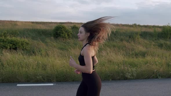 Side View of Young Sports Girl with Long Hair Jogging on Road at Evening Nature