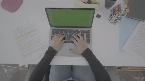 A Young Woman Dressed in Black is Sitting at a Clean Desk Watching a Laptop with a Green Screen alt