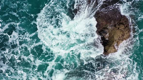 Ocean white waves splashing and foaming on caved cliffs plunged on turquoise sea water, top down aer