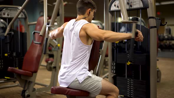 Rear side shot of young bodybuilder doing vertical rear delt fly exercises on a machine.