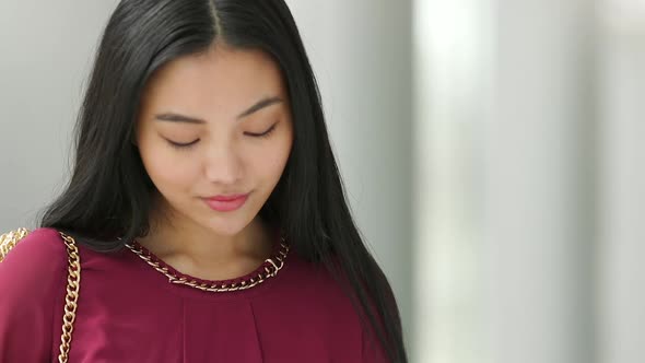 Close up of Asian woman face who is texting then looks up and then continues to text