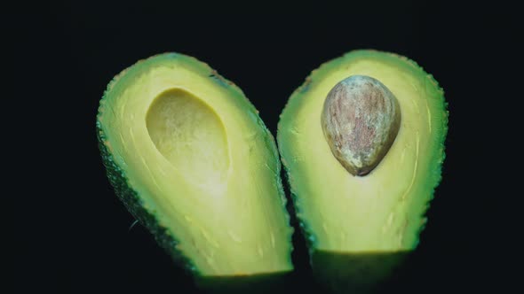 Two Halves of an Avocado Rotate in a Circle on a Black Background