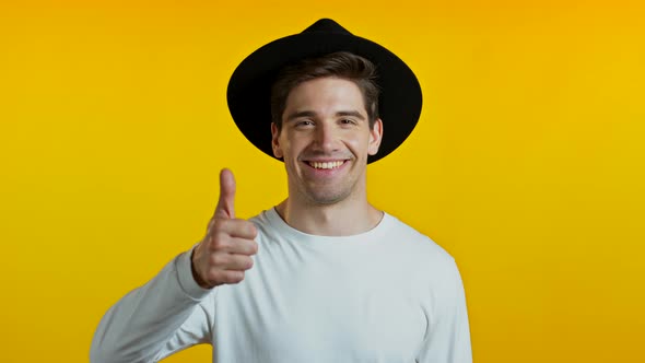Hipster Guy Showing Thumb Up Sign Over Yellow Background. Positive Young Man Smiles To Camera