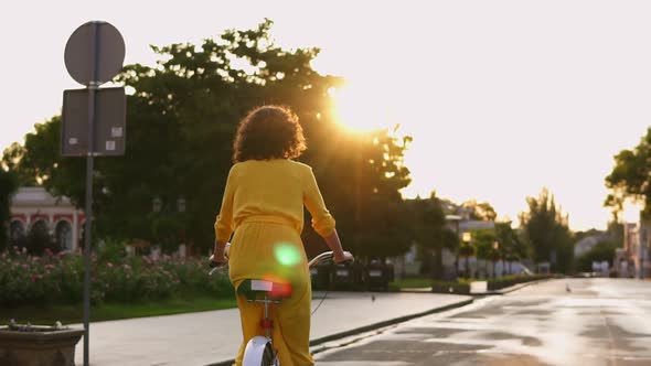 Back View of an Unrecognizable Woman in Long Yellow Dress Riding a City Bicycle in the City Center