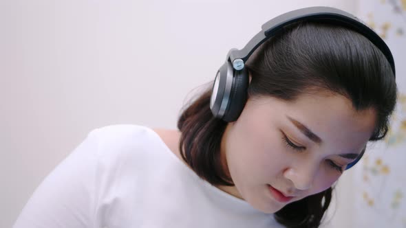Close up Asian beautiful woman using the bluetooth headphone for listening to music so lovely lie in