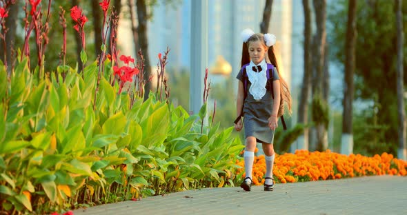 An Elementary School Girl Jumping on a Sidewalk in a Park Near Flowers During Sunset