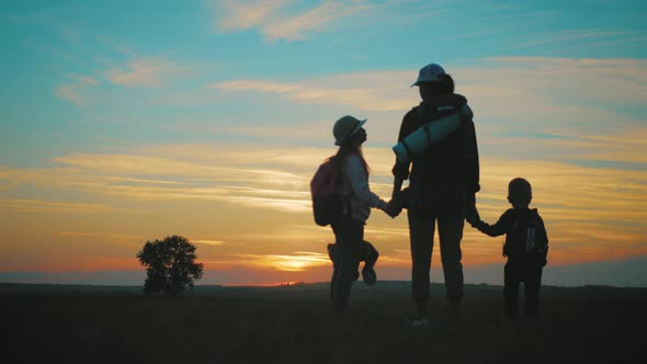 Silhouettes of Mother with Two Kids Hiking on Nature on Sunset. Concept of Friendly Family.