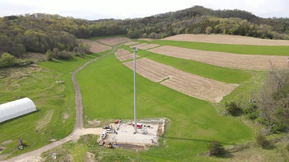 Aerial view of cell tower in rural farm field in valley. Dirt road leading up into the valley.